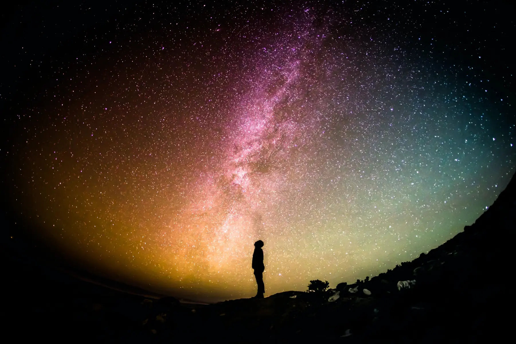 A person standing beneath a vast, colorful night sky filled with stars